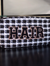 Picture of black and white tweed plaid make-up bag with varsity letter patches spelling out HAIR in black with gold trim