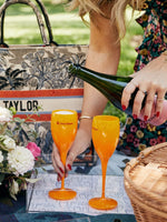 Picture of lady pouring champagne into two Orange Veuve Clicquot Acrylic Champagne Flutes at a picnic